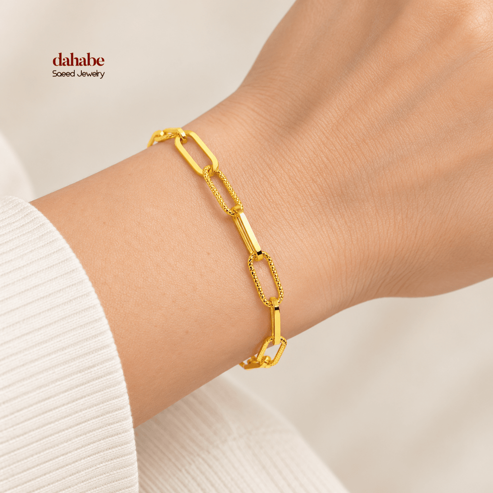 21K yellow gold light paperclip bracelet with alternating textured links and solid bar connectors worn on an adult wrist; AI-generated try-on simulation.